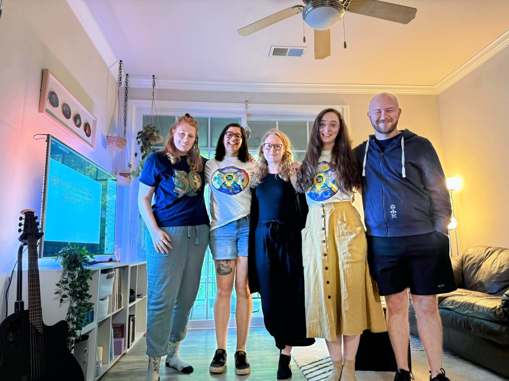 Meg, Nicole, Vendela, Kaley, and Mitchell stand in Meg's living room with Oxonmoot 51 playing in the background