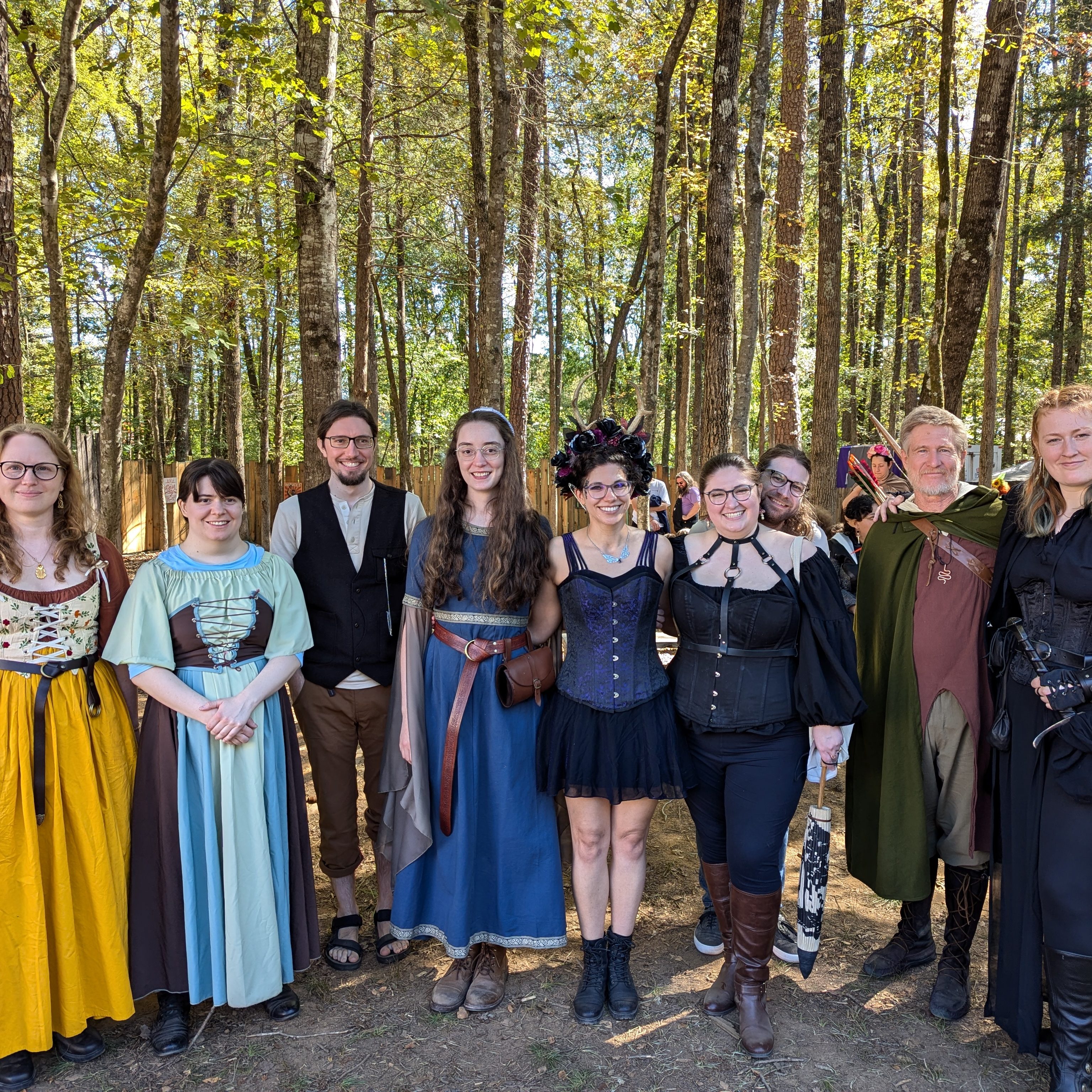 A group of people in Renaissance festival attire stand together in a pretty forested area.